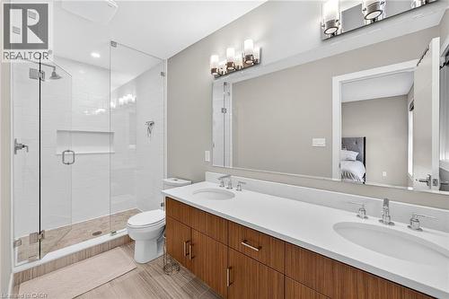 Dual vanity with integrated sinks and wood-finish cabinetry, frameless glass shower enclosure with a built-in niche, and wood-finish flooring - 60 Arkell Road Unit# 57, Guelph, ON - Indoor Photo Showing Bathroom