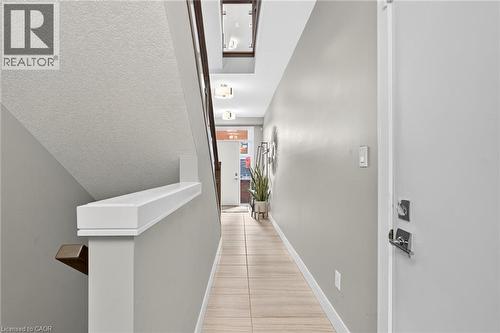 Light-toned wall paint throughout, tile flooring, contemporary wall-mounted light fixtures, and a white stair railing - 60 Arkell Road Unit# 57, Guelph, ON - Indoor Photo Showing Other Room