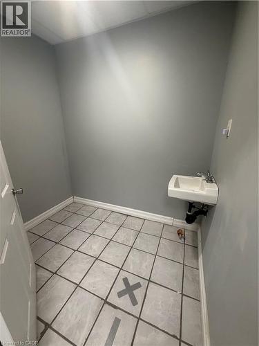 Wall-mounted sink with chrome fixtures, tile flooring, and light gray wall paint - 10 Sanford Avenue N, Hamilton, ON 