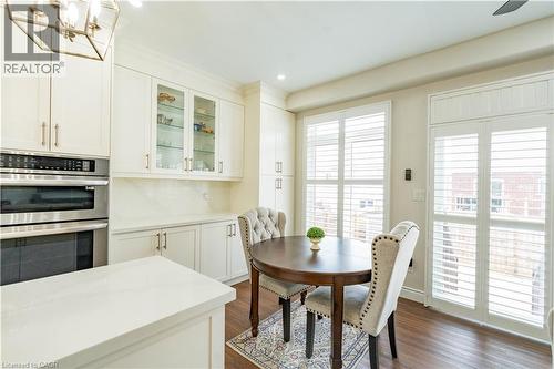 Wood-finish flooring, white cabinetry with glass-front uppers, built-in stainless steel appliances, white countertops, and white plantation shutters - 122 Iron Gate Street, Kitchener, ON - Indoor Photo Showing Dining Room