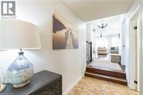 Tiled entry flooring with a wood-finish staircase leading to an open living area featuring wood-finish flooring and a chandelier - 122 Iron Gate Street, Kitchener, ON - Indoor Photo Showing Other Room