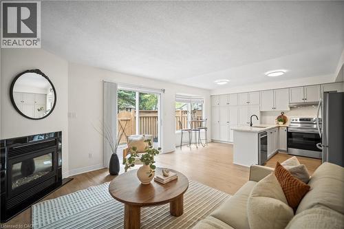 Recessed electric fireplace with black tile surround, wood-finish flooring throughout, sliding glass door to outdoor space, kitchen featuring light gray cabinetry, stainless steel appliances - 320 Hamilton Drive Unit# 10, Ancaster, ON - Indoor Photo Showing Living Room With Fireplace