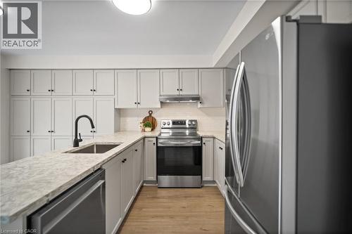 Kitchen featuring light-toned cabinetry, light-toned countertops, stainless steel appliances, a subway tile backsplash, and wood-finish flooring - 320 Hamilton Drive Unit# 10, Ancaster, ON - Indoor Photo Showing Kitchen With Upgraded Kitchen