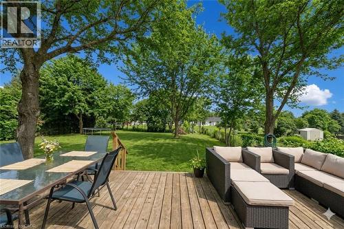 *VIRTUALLY STAGED* Expansive wooden deck with a glass-top dining table, providing access to a large manicured lawn bordered by mature trees - 44 Mcclellan Road, Alton, ON - Outdoor With Deck Patio Veranda