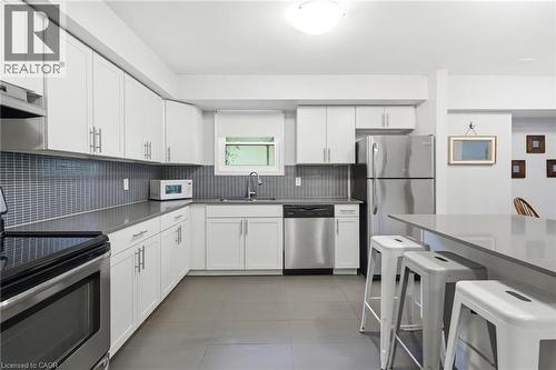 Kitchen featuring white cabinetry, stainless steel appliances, dark countertops, a gray tile backsplash, and a breakfast bar - 509 Quiet Place Unit# 1, Waterloo, ON - Indoor Photo Showing Kitchen With Double Sink