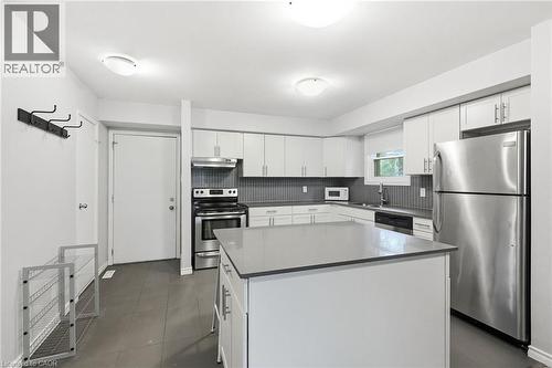 Modern kitchen featuring a central island with a solid surface countertop, white cabinetry, stainless steel appliances, and a grey tile backsplash - 509 Quiet Place Unit# 1, Waterloo, ON - Indoor Photo Showing Kitchen