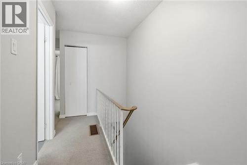 Second-story hallway featuring neutral-toned carpet, a white baluster railing with a wood-finish handrail, and white bi-fold closet doors - 509 Quiet Place Unit# 1, Waterloo, ON - Indoor Photo Showing Other Room