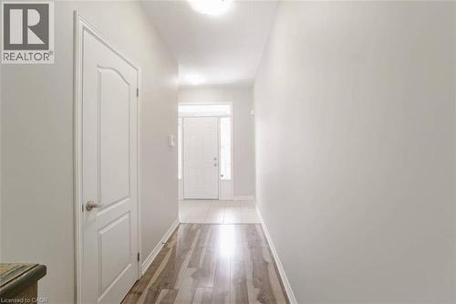 Light wood-finish flooring extending into the hallway, white interior doors with brushed nickel hardware, and a white front entry door with a sidelight - 70 Bradbury Road, Hamilton, ON - Indoor Photo Showing Other Room