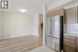 Kitchen featuring wood-finish cabinetry, stainless steel refrigerator, white subway tile backsplash, and light-colored countertops - 