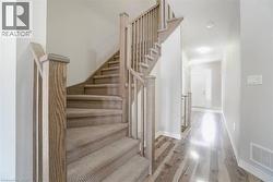 Staircase with wood-finish newel posts and handrails, carpeted treads, and light gray wall paint - 