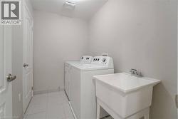 Laundry area with white appliances, utility sink, and light-toned tile flooring - 
