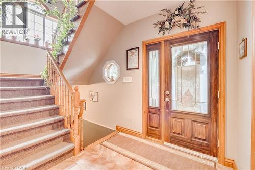 Wood entry door with decorative glass inserts and side panel, wood staircase with carpeted treads, and tiled flooring - 875 Safari Road, Hamilton, ON 