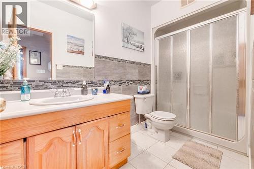 Vanity with integrated sink, wood-finish cabinetry, tile flooring, glass-enclosed shower, and tiled wall accents - 875 Safari Road, Hamilton, ON 