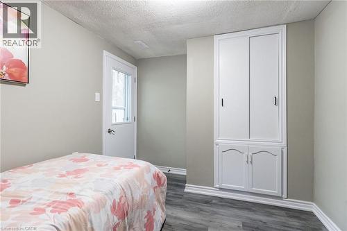 Built-in cabinetry with sliding upper doors and lower arched panel doors, wood-finish flooring, and a white exterior door with glass panels - 15 Spiers Crescent, Cambridge, ON - Indoor Photo Showing Bedroom