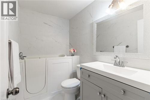Walk-in tub, wall-mounted white tile, framed mirror, vanity with integrated sink, and chrome fixtures - 15 Spiers Crescent, Cambridge, ON - Indoor Photo Showing Bathroom