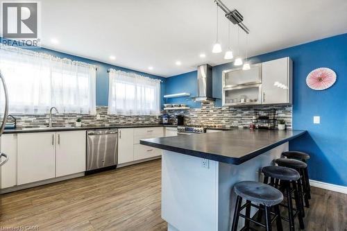 Kitchen featuring wood-finish flooring, white cabinetry, stainless steel appliances, a multi-tone tile backsplash, and an island with counter seating - 510 Oakridge Place, Waterloo, ON - Indoor Photo Showing Kitchen With Upgraded Kitchen