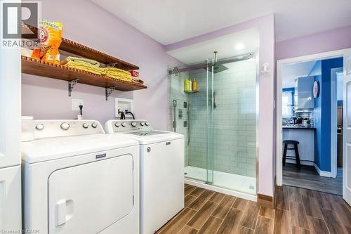 Modern laundry room featuring side-by-side washer and dryer with white finish, wood-finish flooring, and a wooden floating shelf with decorative storage - 510 Oakridge Place, Waterloo, ON - Indoor Photo Showing Laundry Room