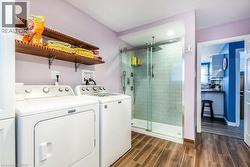 Modern laundry room featuring side-by-side washer and dryer with white finish, wood-finish flooring, and a wooden floating shelf with decorative storage - 