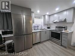 Stainless steel appliances, recessed ceiling lighting, light-toned cabinetry, wood-finish flooring, and a subway tile backsplash - 