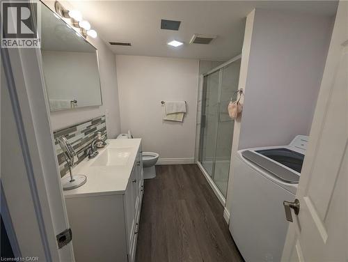 Spacious bathroom featuring a white vanity with integrated sink, glass-enclosed shower, wood-finish flooring, and a modern top-load washer - 510 Oakridge Place, Waterloo, ON - Indoor Photo Showing Laundry Room