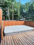 Expansive deck featuring a hot tub, wood privacy fencing, and mature trees - 