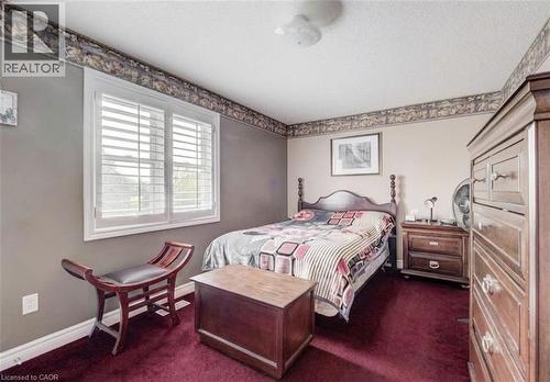 Bedroom featuring a window with white louvered shutters, textured wall covering, deep red carpeting, and a ceiling-mounted light fixture - 599 Coldstream Drive, Waterloo, ON - Indoor Photo Showing Bedroom
