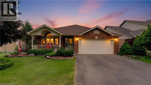 Brick-front residence featuring a covered front porch, an arched window, and a prominent attached garage with a paved driveway - 599 Coldstream Drive, Waterloo, ON - Outdoor With Deck Patio Veranda With Facade