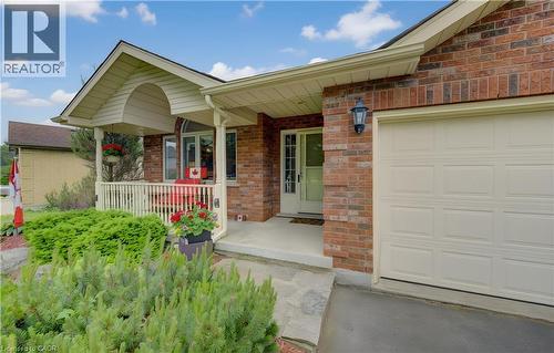Brick exterior featuring a covered front porch with white railing, a single-panel garage door, and mature landscaping - 599 Coldstream Drive, Waterloo, ON - Outdoor With Deck Patio Veranda