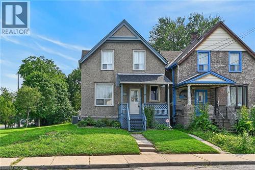 Exterior featuring a gabled roofline, light-colored stucco finish, covered front porch, and a dedicated walkway - 230 Picton Street E, Hamilton, ON - Outdoor With Facade