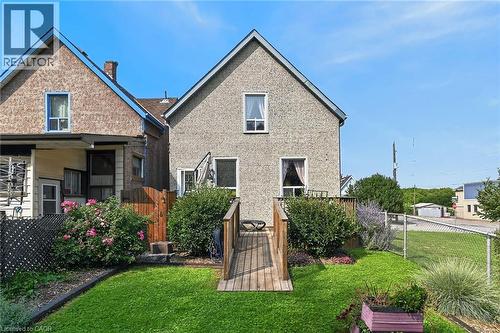 Rear exterior featuring a wooden deck with ramp access, manicured lawn, established shrubs, and a chain-link fence - 230 Picton Street E, Hamilton, ON - Outdoor