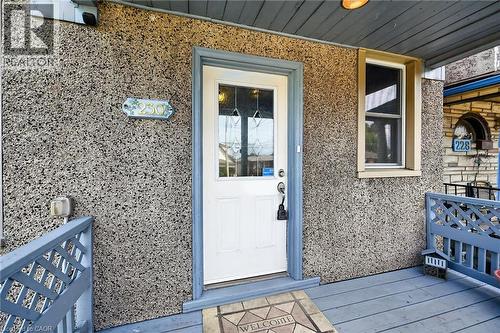 Front entry featuring a white door with decorative glass, a single window with light trim, a textured exterior, and a wooden porch with railing - 230 Picton Street E, Hamilton, ON - Outdoor With Exterior