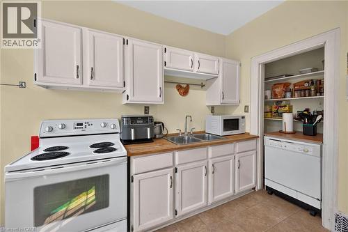 Kitchen featuring white cabinetry, wood-finish countertops, tile flooring, a dual-basin sink, and a built-in pantry with shelving - 230 Picton Street E, Hamilton, ON - Indoor Photo Showing Kitchen With Double Sink