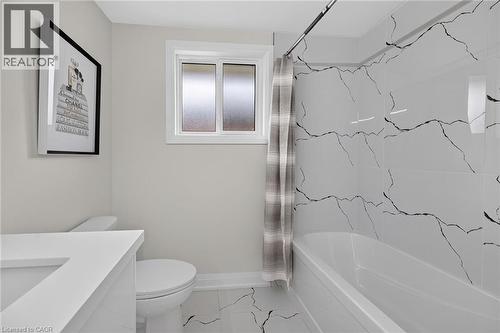 Crisp white bathtub with floor-to-ceiling accent tile, single vanity with integrated sink, and a white toilet - 40 Purdy Crescent, Hamilton, ON - Indoor Photo Showing Bathroom