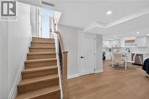 Wood-finish flooring, staircase with wood treads and black metal balusters, recessed lighting, white cabinetry, and stainless steel appliances - 40 Purdy Crescent, Hamilton, ON - Indoor Photo Showing Other Room