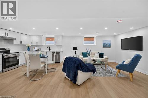 Open-concept living area featuring a kitchen with white cabinetry and stainless steel appliances, wood-finish flooring, recessed lighting, and a wall-mounted display - 40 Purdy Crescent, Hamilton, ON - Indoor