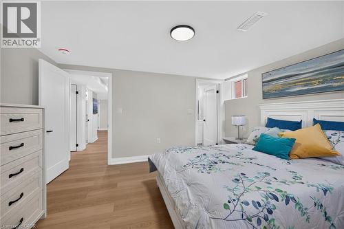 Light wood-finish flooring, white paneled doors with dark hardware, and a window with brick exterior visibility - 40 Purdy Crescent, Hamilton, ON - Indoor Photo Showing Bedroom