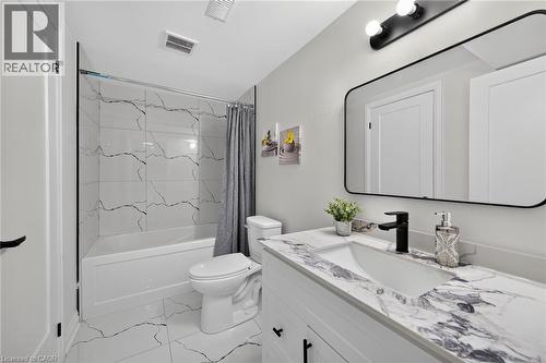 White bathroom featuring a bathtub with a shower, a modern vanity with a single sink, a black-framed mirror, and a black faucet - 40 Purdy Crescent, Hamilton, ON - Indoor Photo Showing Bathroom