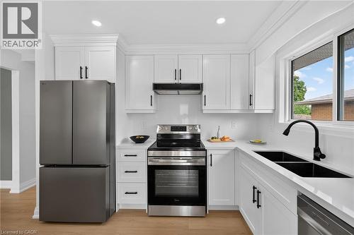 White shaker-style cabinetry with matte black hardware, stainless steel appliances, dual basin undermount sink with matte black faucet, recessed lighting, and wood-finish flooring - 40 Purdy Crescent, Hamilton, ON - Indoor Photo Showing Kitchen With Double Sink