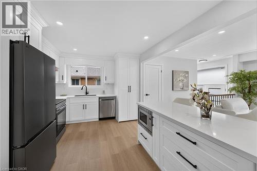 Modern kitchen featuring white cabinetry, light wood-finish flooring, a stainless steel dishwasher, a built-in microwave, and a white countertop - 40 Purdy Crescent, Hamilton, ON - Indoor Photo Showing Kitchen
