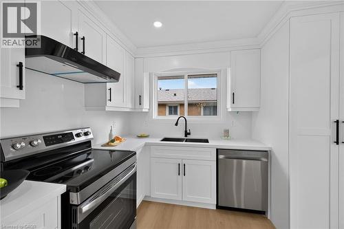 Kitchen featuring white cabinetry, stainless steel appliances, a black sink, and wood-finish flooring - 40 Purdy Crescent, Hamilton, ON - Indoor Photo Showing Kitchen