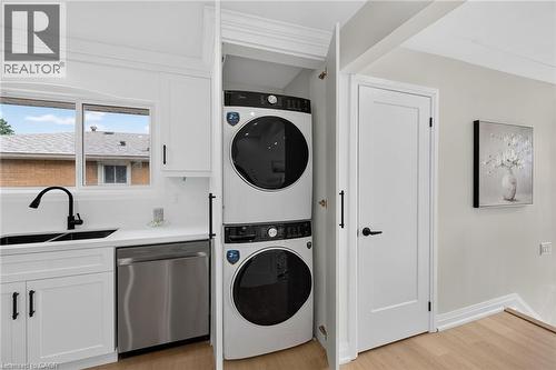 White cabinetry with black hardware, stainless steel dishwasher, a black gooseneck faucet with an undermount sink, and wood-finish flooring - 40 Purdy Crescent, Hamilton, ON - Indoor Photo Showing Laundry Room