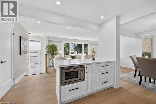 White kitchen island with a built-in microwave, light wood-finish flooring, recessed lighting, expansive windows, and a doorway with frosted glass panels - 40 Purdy Crescent, Hamilton, ON - Indoor