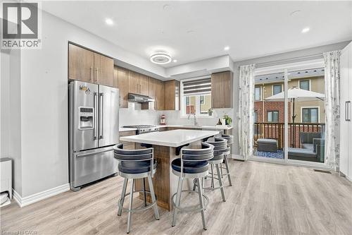 Modern kitchen featuring wood-finish cabinetry, stainless steel appliances, a white countertop island, and wood-finish flooring - 1890 Rymal Road E Unit# 144, Hamilton, ON - Indoor