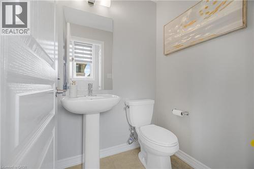 Pedestal sink with chrome faucet, wall-mounted mirror, overhead vanity lighting, and a window with blinds - 1890 Rymal Road E Unit# 144, Hamilton, ON - Indoor Photo Showing Bathroom