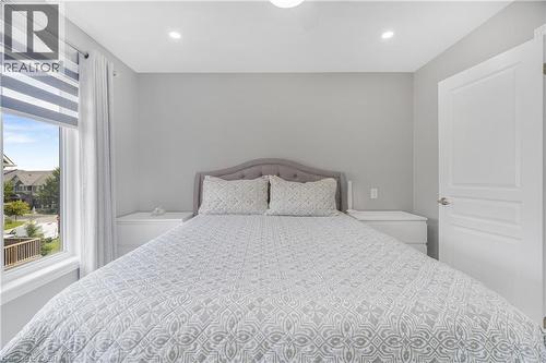 Bright secondary bedroom featuring a curved upholstered headboard, recessed ceiling lighting, large windows with motorized roller shades, and direct access to a covered outdoor balcony overlooking the - 1890 Rymal Road E Unit# 144, Hamilton, ON - Indoor Photo Showing Bedroom
