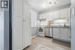 Kitchen featuring white cabinetry, stainless steel dishwasher, white range with coordinating range hood, and wood-finish flooring - 