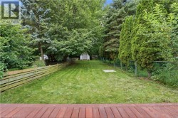 Expansive grassy yard enclosed by a wood-plank fence and a chain-link fence, featuring mature perimeter trees and a visible storage shed - 