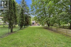 Expansive backyard with a manicured lawn, established trees, and a wooden privacy fence - 