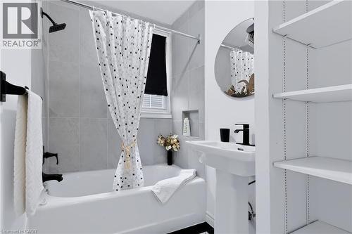 White bathtub with a matte black shower fixture, pedestal sink with a matte black faucet, and built-in shelving - 703 Brighton Avenue, Hamilton, ON - Indoor Photo Showing Bathroom