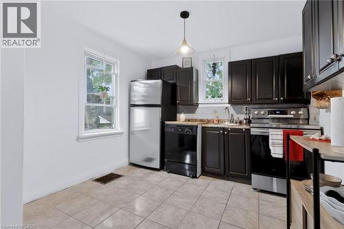 Kitchen featuring dark wood cabinetry, light tile flooring, stainless steel oven, white tile backsplash, and a pendant light fixture - 703 Brighton Avenue, Hamilton, ON - Indoor Photo Showing Kitchen